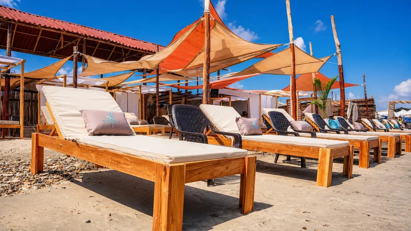 Fila de camastros de madera con cojines de marca y velas de sombra en Nakawa Beach Club.