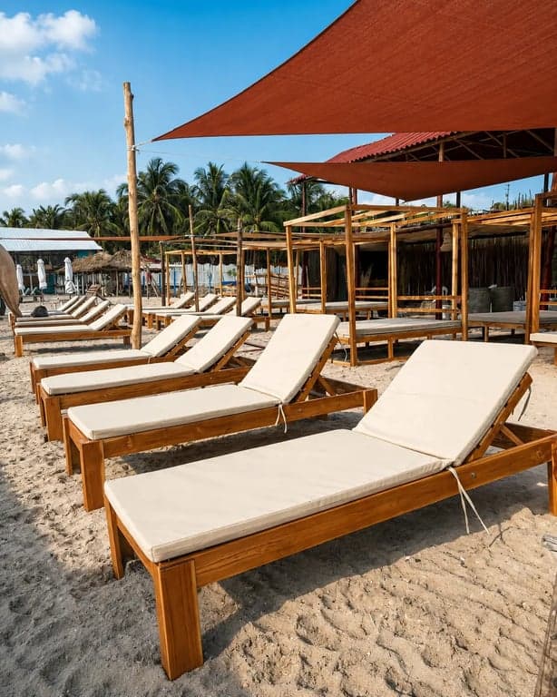 Camastros de madera con colchoneta bajo vela terracota y palmeras en Nakawa Beach Club.
